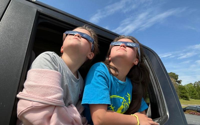 Pictured from left is eight-year-old Dalis McDonald and 11-year-old Cashtyn McDonald watching the eclipse in the car rider pick up line at North Hart Elementary School.